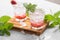 Two glasses with summer strawberry soda drink or mojito with strawberry, ice cubes and mint leaves on light background