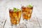 Two glasses with traditional iced tea with lemon, mint leaves and ice cubes in glass on rustic wooden table