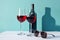 two glasses of wine and a bottle of wine on a table with a shadow of a bottle and a pair of sunglasses on the table