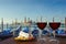 Two glasses of wine with charcuterie assortment on view of gondolas and San Giorgio Maggiore church in the background in Venice.