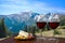 Two glasses of wine with cheese and meat assortment on view of mountains landscape. Glass of red wine with different snacks -