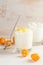 Two glasses with  yogurt, one standing spoon, whole and cut kumquats on white table on light background.