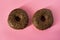 Two glazed chocolate donuts on pink background - minimalism, copy space