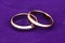Two gold wedding rings. Engagement rings close up on violet velvet background, macro jewelry for newlyweds