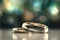 Two gold wedding rings are in front of a bokeh background, in the style of digitally enhanced, light green