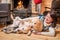 Two golden Labrador retriever dogs lie with a middle-aged Asian woman on blanket in front of country house fireplace