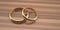 Two golden wedding rings are large below and small above on a wooden table background