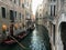 Two gondoliers navigating their gondolas down a narrow quiet canal in Venice, Italy through the old Venetian homes.