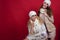 Two gorgeous girlfriends with perfect smiles wearing white woolen hats, scarves, sweaters and waistcoats in the red background