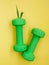 two green heavy dumbbells with leaves in shape of Easter bunny on yellow background. Easter fitness and training