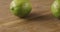 Two green limes roll on a wooden table