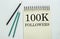 Two green one black pencil with text 100K Followers in the notebook on the white background