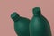 Two green opaque bottles or flasks on a pink background