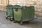 Two Green Trash Dumpsters In Front Of White Brick Wall Angle View. Green recycling dumpsters against a brick wall