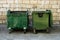 Two Green Trash Dumpsters In Front Of White Brick Wall Front View With Room For Text. Garbage Cans in Front of Warehouse Wall.