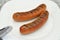 Two Grilled Sausages on white Plate