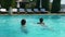 Two guys jump into the swimming pool and enjoy a nice swim while girl sits on the edge