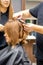 Two hairstylists make curls hairstyle of long brown hair with the curling iron in hairdresser salon.