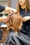 Two hairstylists make curls hairstyle of long brown hair with the curling iron in hairdresser salon.