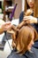 Two hairstylists using curling iron on customers long brown hair in a beauty salon.