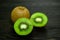 Two halves bright juicy ripe beautiful kiwi and a whole kiwi on a coarse dark wooden background from boards