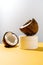 Two halves of coconut and a jar of cosmetics on a yellow and gray background.