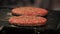 Two hamburger patties seasoned with salt and pepper grilling on a black metal grill
