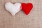 Two handmade fabric hearts clipped with clothespin on sackcloth,