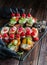 Two hands in black gloves holding a snack tray on woody background: rolls, canapes, rolls, stuffed tomatoes, sandwich with caviar