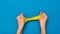 Two hands on a blue background stretch a bright yellow slime.