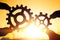 Two hands holding gears together. puzzle details on a sunset background.