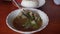 Two hands stir a steaming bowl of Soto Otot or tendon soup