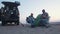 Two handsome friends campers sits on campers chairs near the tent, plays guitar and sings