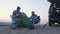 Two handsome friends campers sits on campers chairs near the tent, plays guitar and sings