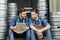 Two handsome guys in aprons talking and looking at tablet, near metal barrels