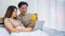 Two happy Asian man and woman sitting together on a bed. They enjoy looking at a laptop on a wife`s lap while a husband holds a