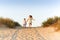 Two happy cheerful little sisters running hand in hand on sand on sunny evening beach