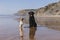 two happy dogs having fun at the beach. Sitting on the sand with reflection on the water at sunset. Cute small dog and black