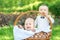 Two happy fancy little infants in white suits with bow ties sitting in a big wicker basket outdoor in a sunny spring or summer day