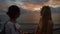 Two happy female travelers talking and laughing at the sunset against a background of the sea. Blonde and brunette are