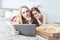 Two happy girls in pajamas spending time together at bachelorette party, using digital tablet and eating pizza in bed.