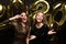 Two happy girls in shiny dresses posing while standing with gold colored 2020 number balloons on black background