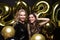 Two happy girls in shiny dresses posing while standing with gold colored 2020 number balloons on black background