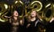 Two happy girls in shiny dresses posing while standing with gold colored 2020 number balloons on black background