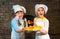 Two happy kids in chef hats hold pizza together on a stone stove background.