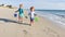 Two happy little Caucasian kids run with toy buckets on beach