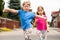 Two happy little children, sisters, siblings walking, girls jumping happily towards the camera with arms spread wide. Kids, family