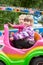 Two happy little girls having fun in outdoor amusement park with riding in car on carousel, driving with steering wheel