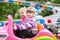 Two happy little girls having fun in summer amusement park with riding on car on carousel, driving with steering wheel