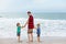 Two happy little kids boys and father standing on the beach of ocean and looking on horizon on stormy day. Family, dad